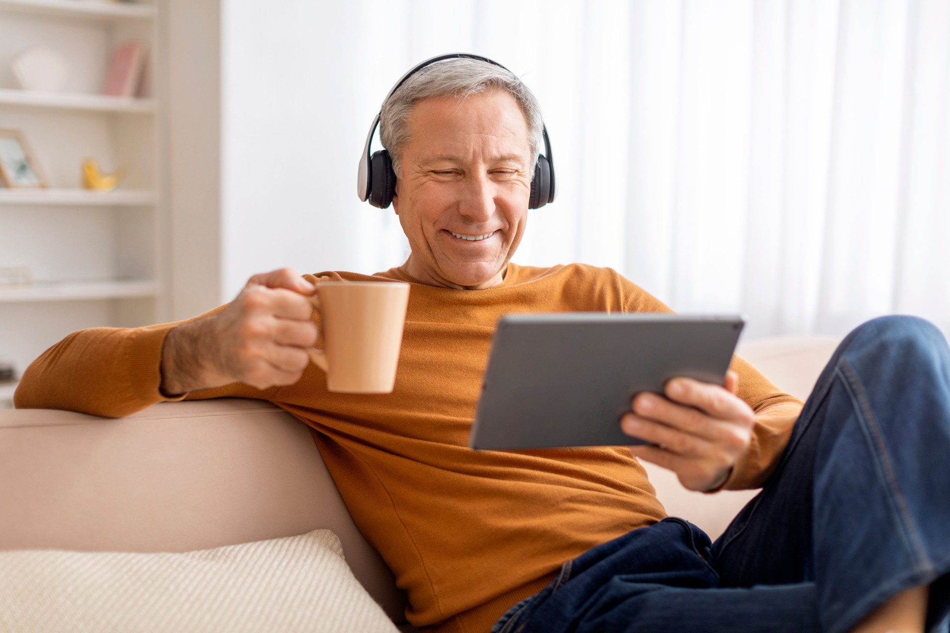 Relaxed elderly man chilling at home, using tablet and headphones